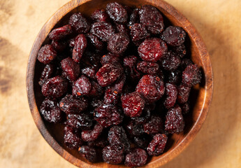 Dried cranberries in a wooden bowl on a wooden background.