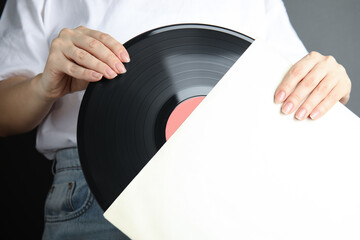 Woman taking vinyl record out of paper sleeve on grey background, closeup