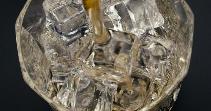 Camera follows liqueur jet, while drink is pouring into the glass with cold ice