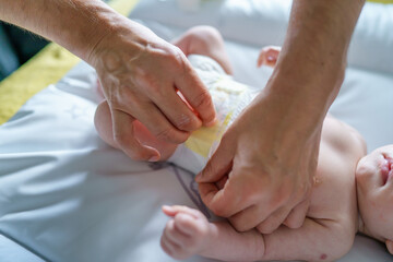Close up on hands of unknown man while taking care of his baby child changing diapers on bed at...