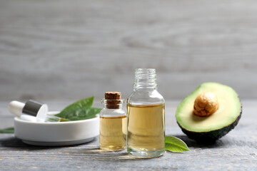 Bottles of essential oil and fresh avocado on grey wooden table