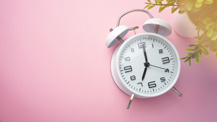 Analog alarm clock and artificial flower on pink background.
