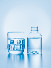 Glass with ice and small plastic bottle of drink water on sky blue background