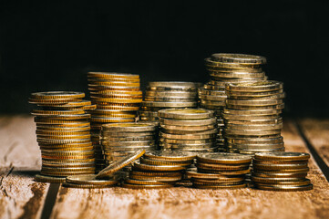 Coins set up in rows of high and low elevation patterns are placed together on an old wooden tabletop and black background.