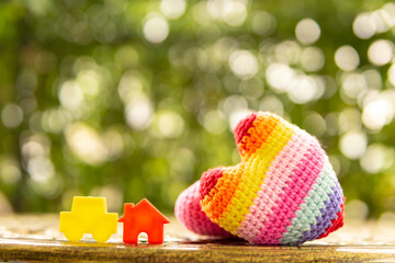 Hand are hold rainbow heart and home model.Give love to the family for happiness..Have background in garden and light of sun.