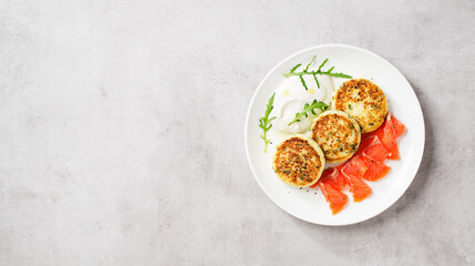 Salted cottage cheese pancake with greens, served with smoked salmon slices and sour cream. Healthy breakfast. Light gray background.Top view. Space for text