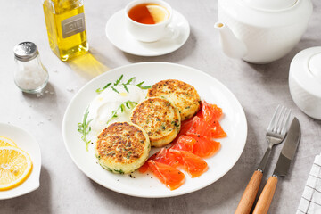 Salted cottage cheese pancake with greens, served with smoked salmon slices and sour cream. Healthy breakfast. Light gray background.