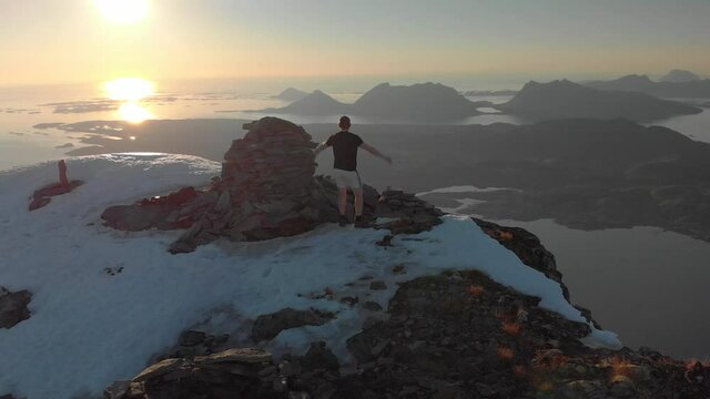 4K orbit motion drone shot on beautiful mountain with man raising arms to the sky. Panorama sunset at golden hour in Northern Norway breathtaking landscape at Helgeland