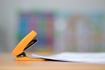 Orange stapler that is stapled together for easy storage on a light brown table.