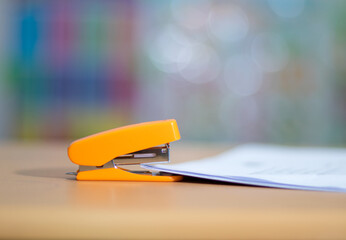 An orange stapler that sits on the desk ready for stapling the papers in a series of arrangements.