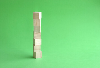 7 letter blank and wood block stacked up, green background. Copy space.
