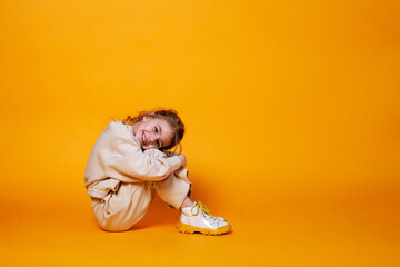 Cute little girl sitting on a yellow background. Space for text.