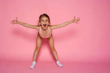 Happy little girl dancing in a  leotard on a pink background. Space for text.