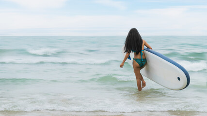 woman surfer in bikini with surfboard walking  to sea for surfing