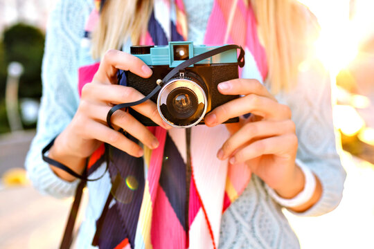 Close up image of woman holding retro vintage film camera, pastel colors sweater and colorful silk scarf, hand details, evening sunlight, bright colors, photographer hobby.
