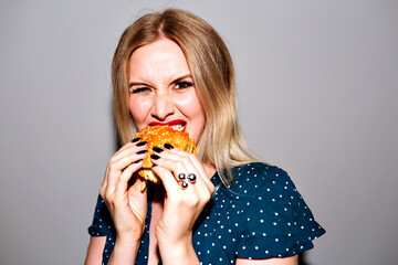 Indoor bright flash image of woman eating big junky burger,