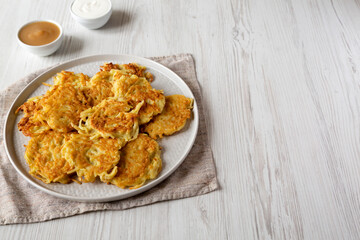Homemade Potato Pancakes Latkes with Apple Sauce and Sour Cream on a white wooden surface, side view. Copy space.