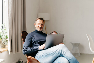 Casual cheerful man relaxing at home with a laptop