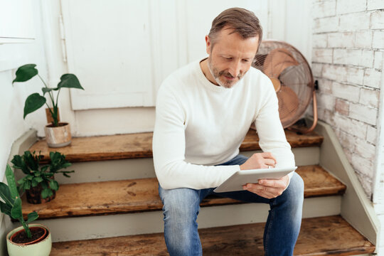 Athletic casual middle-aged man sitting reading on a tablet-pc