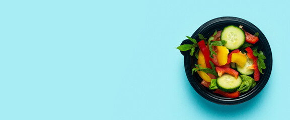 Vegetable salad in a plastic disposable bowl on a light blue background. Top view, flat lay. Banner