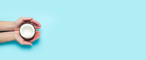 Female palms hold an open half of a coconut on a blue background. Top view, flat lay. Banner
