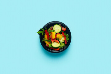 Vegetable salad in a plastic disposable bowl on a light blue background. Top view, flat lay