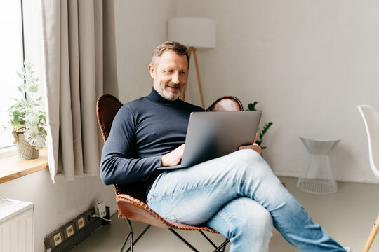 Casual middle-aged man in jeans relaxing with his laptop