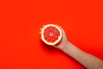 A female hand holds half a grapefruit on a red background. Top view, flat lay. Banner