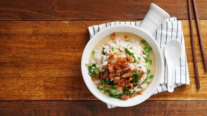 Porridge with spiced pork porridge Garnish with spring onions, coriander, sauteed cabbage, and fried garlic in a baking cup with handle on a wooden table.