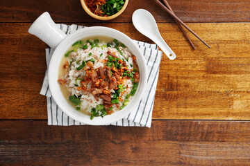 Porridge with spiced pork porridge Garnish with spring onions, coriander, sauteed cabbage, and fried garlic in a baking cup with handle on a wooden table.
