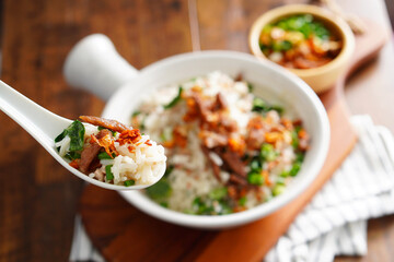 Porridge with spiced pork porridge Garnish with spring onions, coriander, sauteed cabbage, and fried garlic in a baking cup with handle on a wooden table.