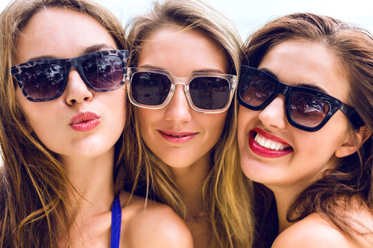 Close up portrait of three funny pretty young women smiling sending kiss and having fun in summer time, fresh fashion  portrait of girls friends wearing sunglasses.