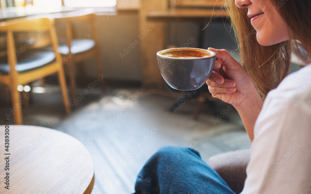 Wall mural closeup image of a beautiful young asian woman holding and drinking hot coffee