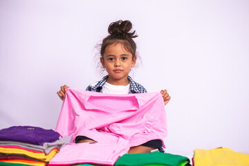 A boy wearing a plaid shirt holding a pink shirt swinging in a pile of colorful shirts .in a white background.The concept of independent play of the child..