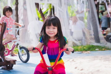 Cute Asian girl riding a tricycle. Happy child wear colorful dresses. Kid smile sweetly. Children...