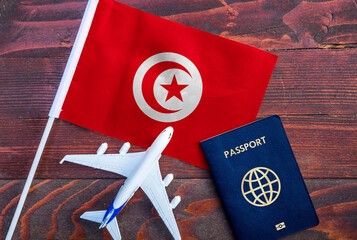 Flag of Tunisia with passport and toy airplane on wooden background. Flight travel concept

