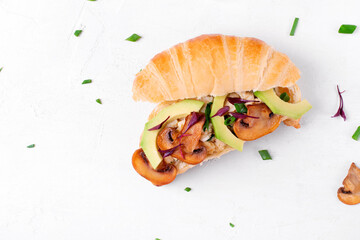 Croissant sandwich with scrambled eggs, roasted mushrooms, avocado and cream cheese on the white table