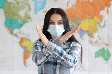 Woman in protective medical mask showing prohibiting gesture against background of world map