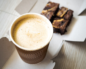 Top view of takeaway paper cup mix hot cappucino coffee foam served with freshly baked brownies.