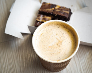 Top view of takeaway paper cup mix hot cappucino coffee foam served with freshly baked brownies.