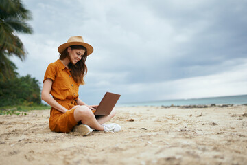 woman in hat with laptop sitting on the beach vacation island