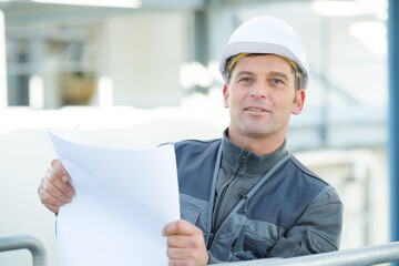 engineer outdoor in helmet holds a plan in hand