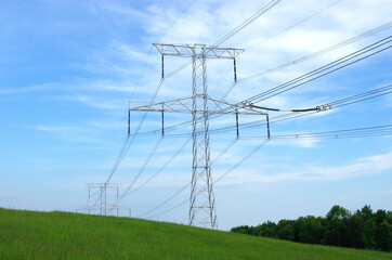 High voltage eletrical towers and lines with blue sky and green meadow. Eletricity towers on a...