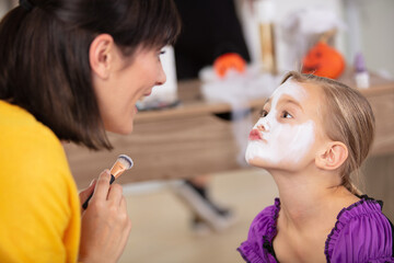 child wearing white face paint pouting lips at her mum