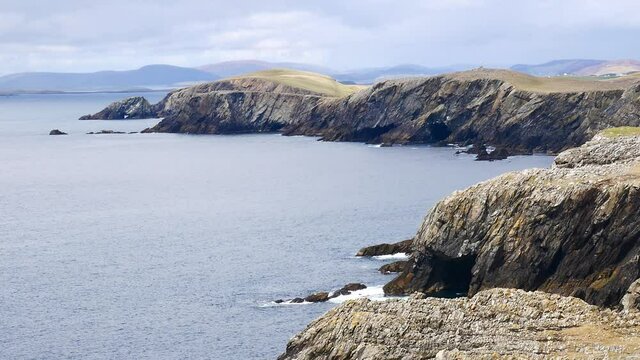 A static shot of the rugged coastal  cliffs making up the coastline on Kenna Ness on the west side of Mainland, Shetland, UK. Waves break on the rocks at the foot of the high cliffs.