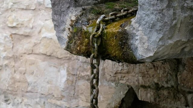 Wasser flie&szlig;t aus einem Brunnen in einer Rinne mit einer Kette