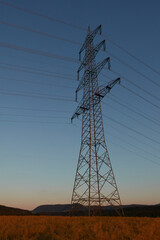 Large Electricity pylon also overhead line pylon stands in the plant field, in the background there are green trees and the hill of the beautiful Swabian Alb can be seen. Germany.