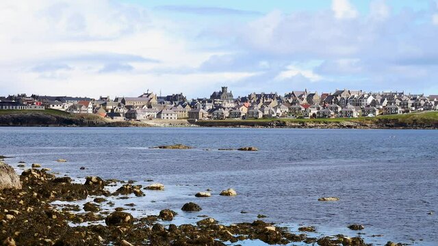 From the Ness of Sound across Brei Wick, a static shot of the skyline of Lerwick, the main town and port of Shetland in the north of the UK. Taken on a sunny day in spring with blue sky and clouds.