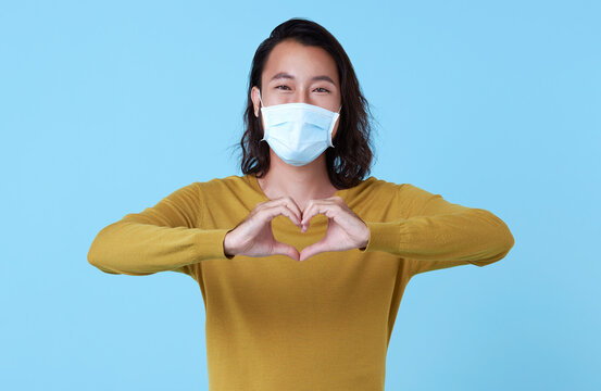 Portrait of young Asian man wearing face mask protecting from Corovavirus isolated on blue studio background.