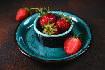Ripe garden strawberry in blue plate on dark stone table